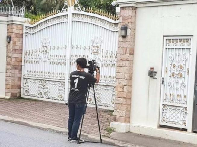 Một phóng viên đứng chờ săn tin trước cổng nhà bà Yingluck