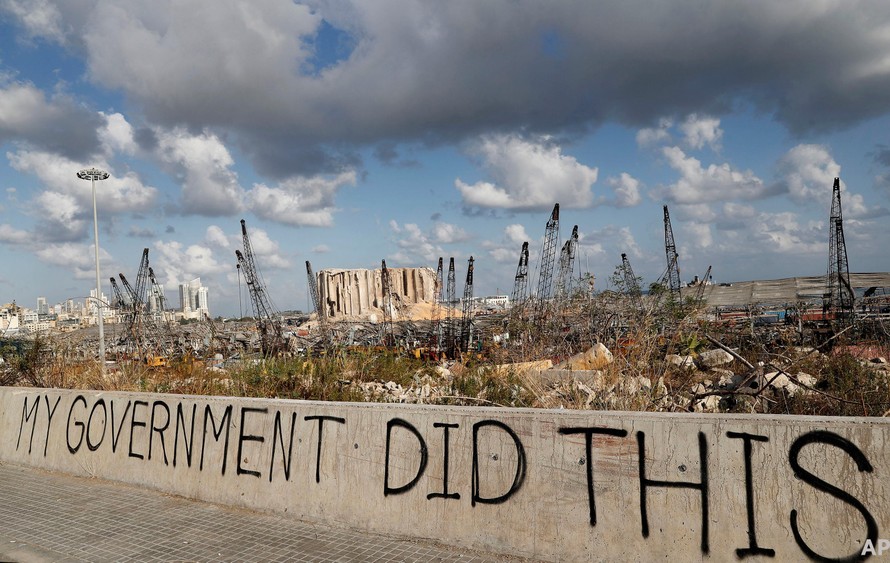 Dòng chữ tố cáo chính phủ Lebanon được viết trên 1 bức tường tại cảng Beirut sau vụ nổ kinh hoàng ngày 4/8/2020. Đắng sau là khung cảnh hoang tàn mà vụ nổ gây ra. (Ảnh: AP)