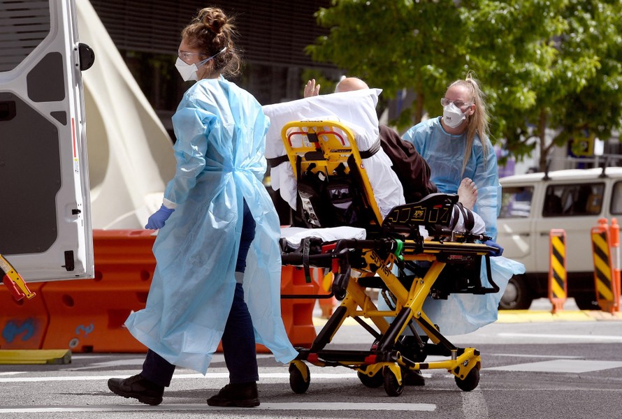Nhân viên y tế chuyển bệnh nhân COVID-19 tới bệnh viện tại Melbourne, Australia. (Ảnh: AFP/TTXVN)