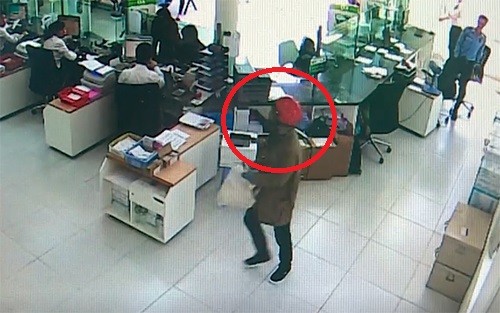 Tên cướp (khoanh tròn đỏ) cầm bao tải trắng tiến thẳng vào quầy gom tiền. Ảnh: Cắt từ video.