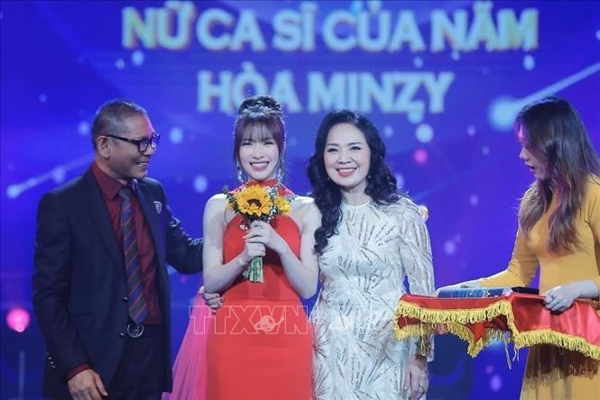 NSND Đức Long và NSND Thái Bảo trao giải thưởng hạng mục "Nữ ca sĩ của năm" cho ca sĩ Hoà Minzy. Ảnh: TTXVN