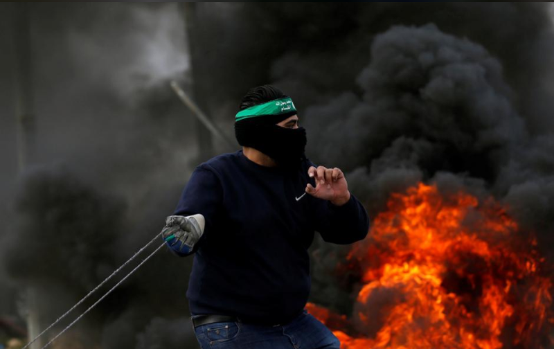 Người dân Palestine ném đá về phía binh sĩ Israel trong cuộc đụng độ biểu tình gần TP Ramallah ở Bờ Tây ngày 19-12, phản đối quyết định của Tổng thống Mỹ Donald Trump công nhận Jerusalem là thủ đô của Israel. Ảnh: REUTERS