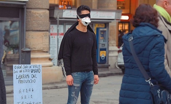 Jian chọn cách bịt mắt, đeo khẩu trang và đứng cạnh tấm biển với nội dung: "Tôi không phải virus, tôi là một con người, hãy xóa bỏ định kiến".