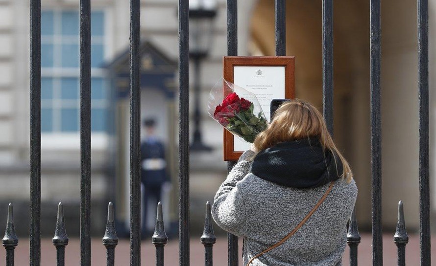 Một người phụ nữ đem theo hoa tới đặt trước cửa Cung điện Buckingham để tưởng nhớ Hoàng tế Philip. Ảnh: AP