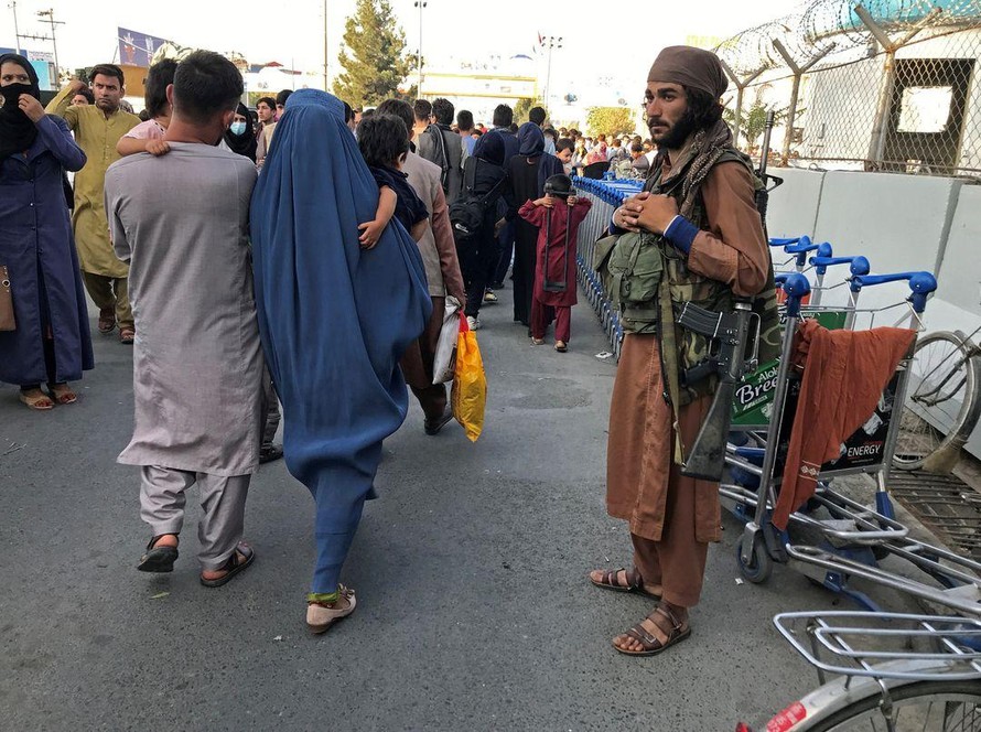 Một tay súng Taliban đứng nhìn người dân đi về phía cổng vào của sân bay quốc tế Hamid Karzai ở Kabul, Afghanistan. Ảnh: Reuters