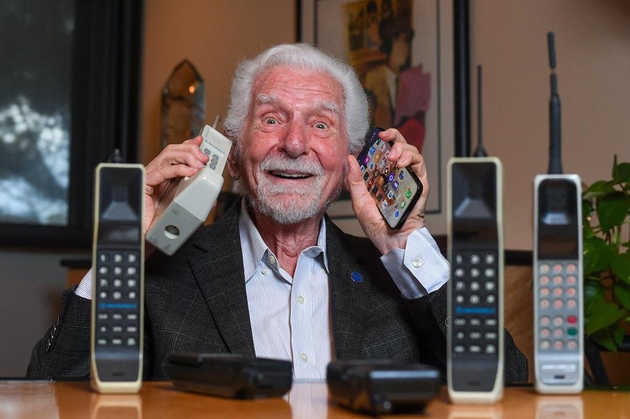 Kỹ sư Martin Cooper cầm trên tay chiếc điện thoại di động đầu tiên được sáng chế vào năm 1973 và mẫu iPhone mới nhất. Ảnh: AFP