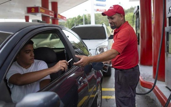 Nhân viên trạm xăng nhận thuốc lá từ một tài xế sau khi bơm xăng ở ngoại ô Caracas hôm 8/10 (Ảnh: AP).