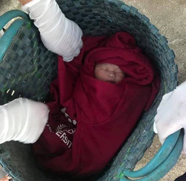Bé trai sơ sinh được quấn trong chiếc áo ấm màu đỏ và để trong chiếc túi màu xanh, bỏ trước nhà một người dân.