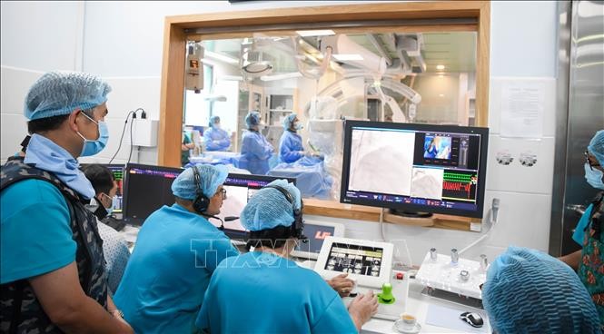 Các bác sĩ điều khiển robot từ bên ngoài để can thiệp mạch vành cho bệnh nhân bên trong phòng can thiệp.
